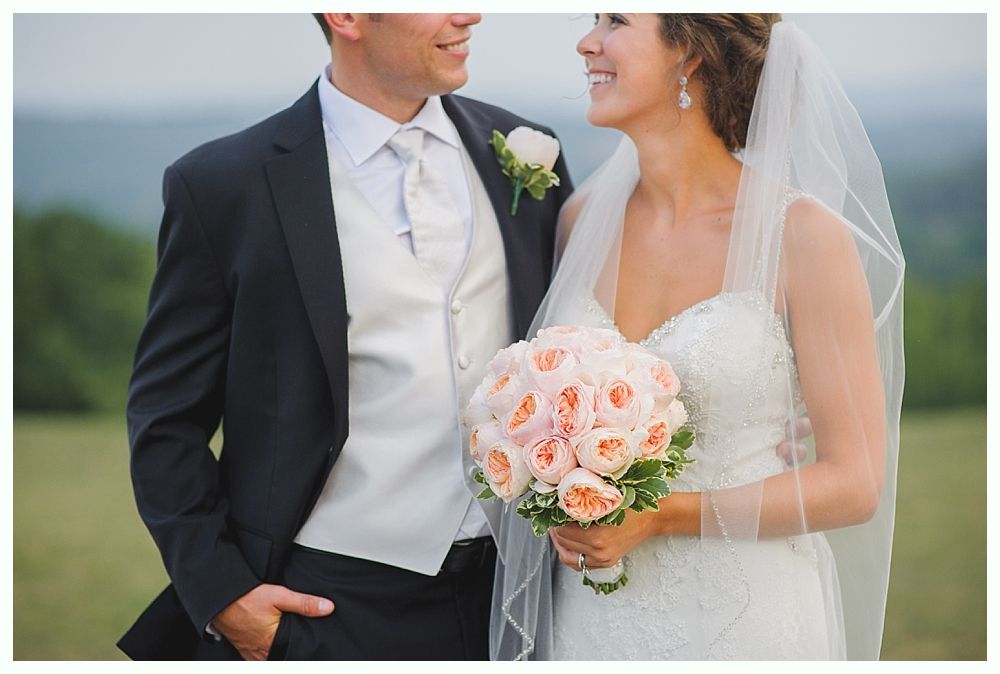 Bride with arms up, making a funny face, groom looking at his hand, cake cutting in background.