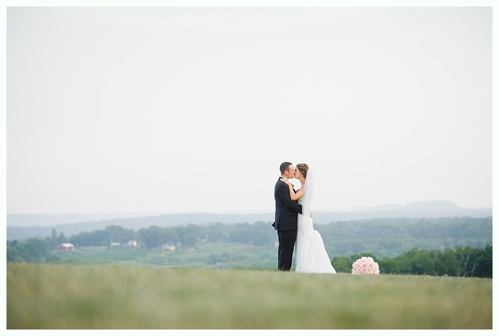 Bride with arms up, making a funny face, groom looking at his hand, cake cutting in background.