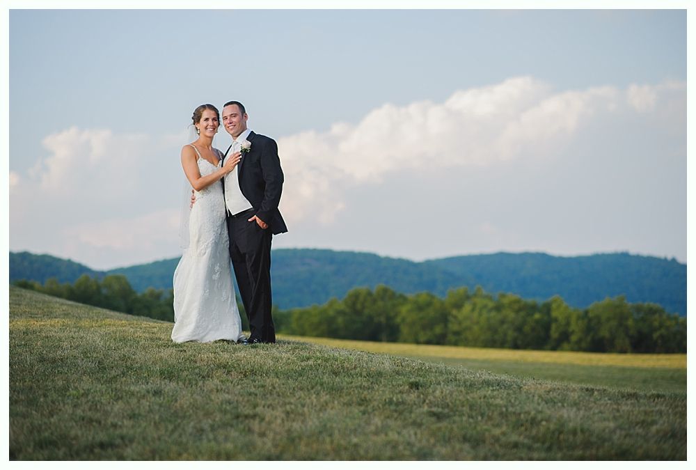 Bride with arms up, making a funny face, groom looking at his hand, cake cutting in background.