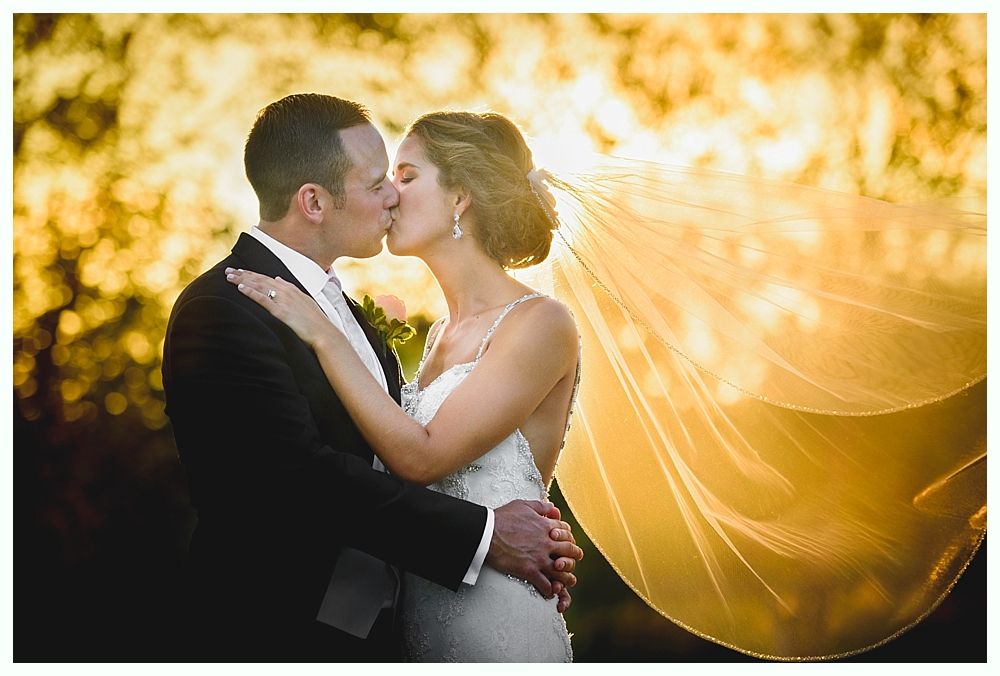 Bride with arms up, making a funny face, groom looking at his hand, cake cutting in background.