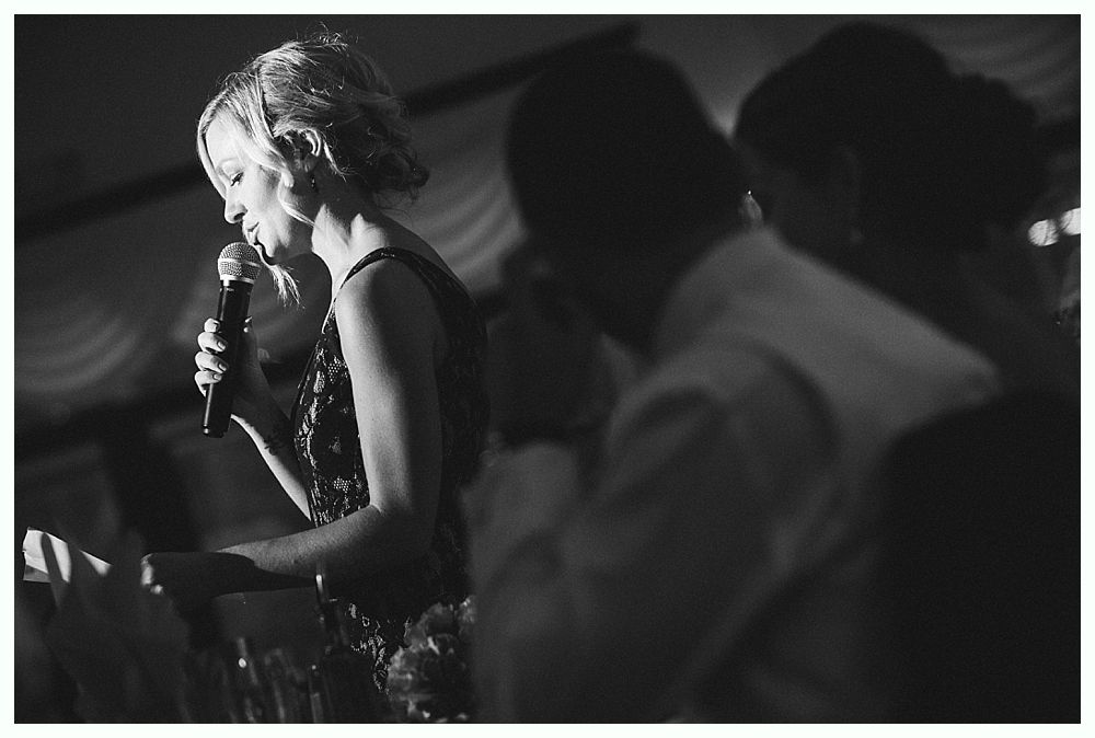 Bride with arms up, making a funny face, groom looking at his hand, cake cutting in background.