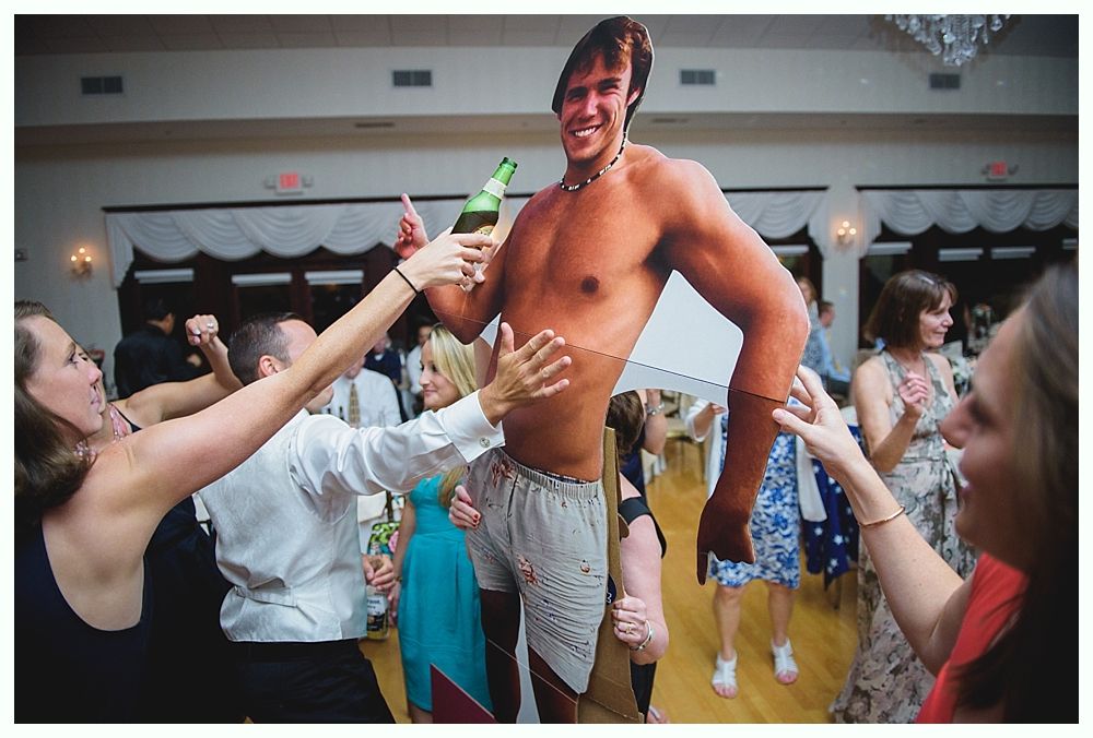 Bride with arms up, making a funny face, groom looking at his hand, cake cutting in background.