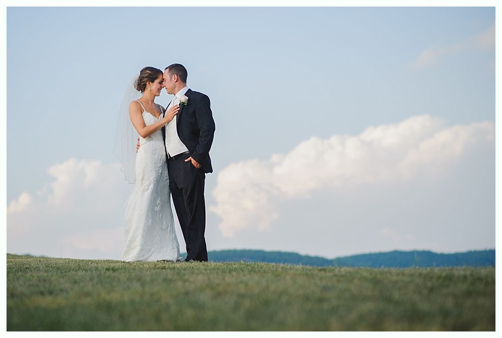 Bride with arms up, making a funny face, groom looking at his hand, cake cutting in background.