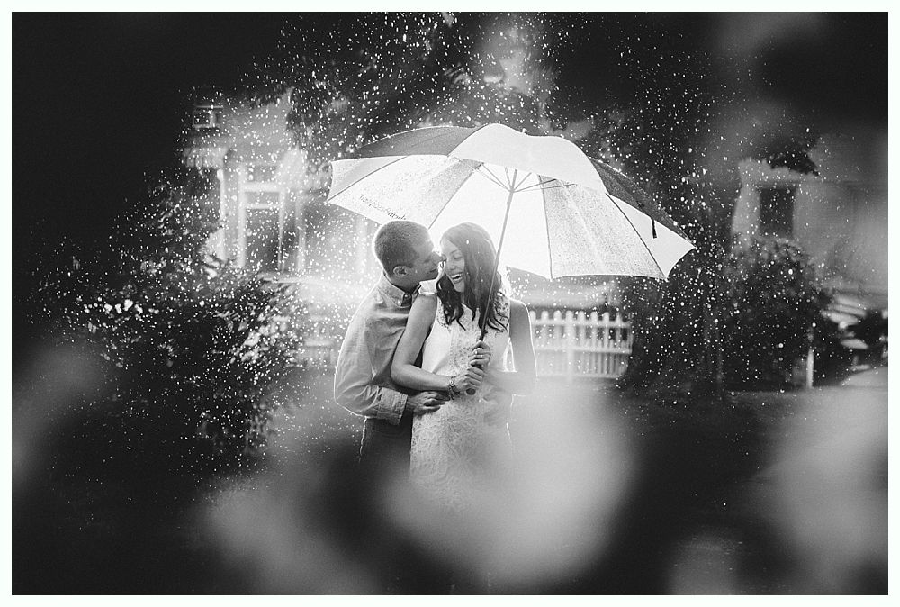 Bride with arms up, making a funny face, groom looking at his hand, cake cutting in background.