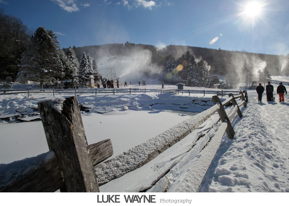 Woman in a button-down shirt adjusts a headpiece, looking at her reflection in a mirror. Black and white photo.