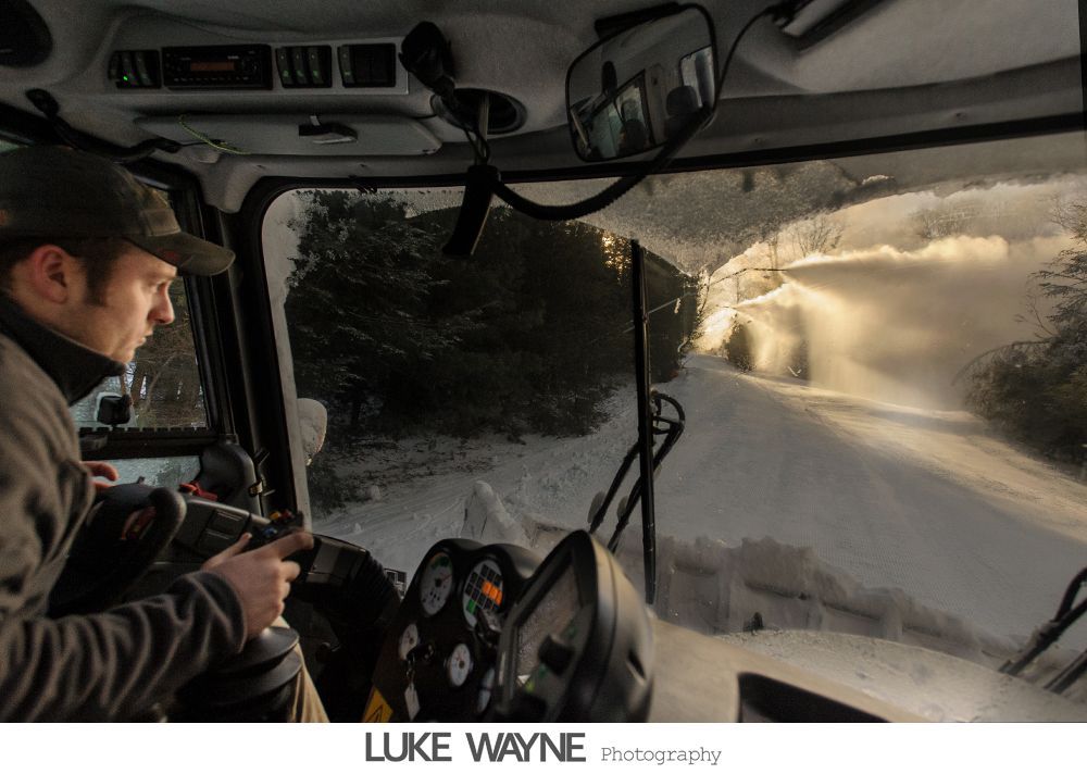Six men in suits pose on steps by a street. One man has arms open, others smile or look at the camera. A bus and car are in the background.