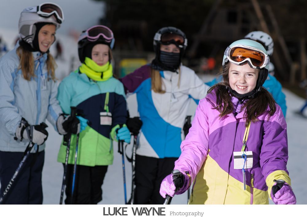 Bride and groom walk down sidewalk, groom smiles, bride holds purple bouquet, city background.