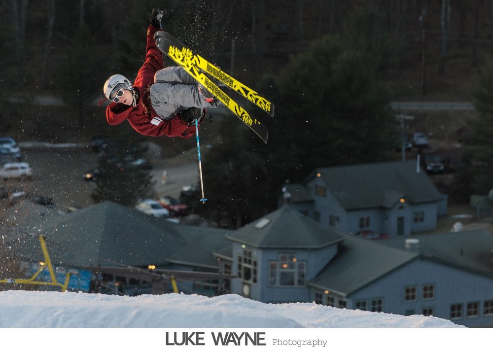 Bride in a fluffy white dress at a bar, smiling. Dark interior, fluorescent lights.