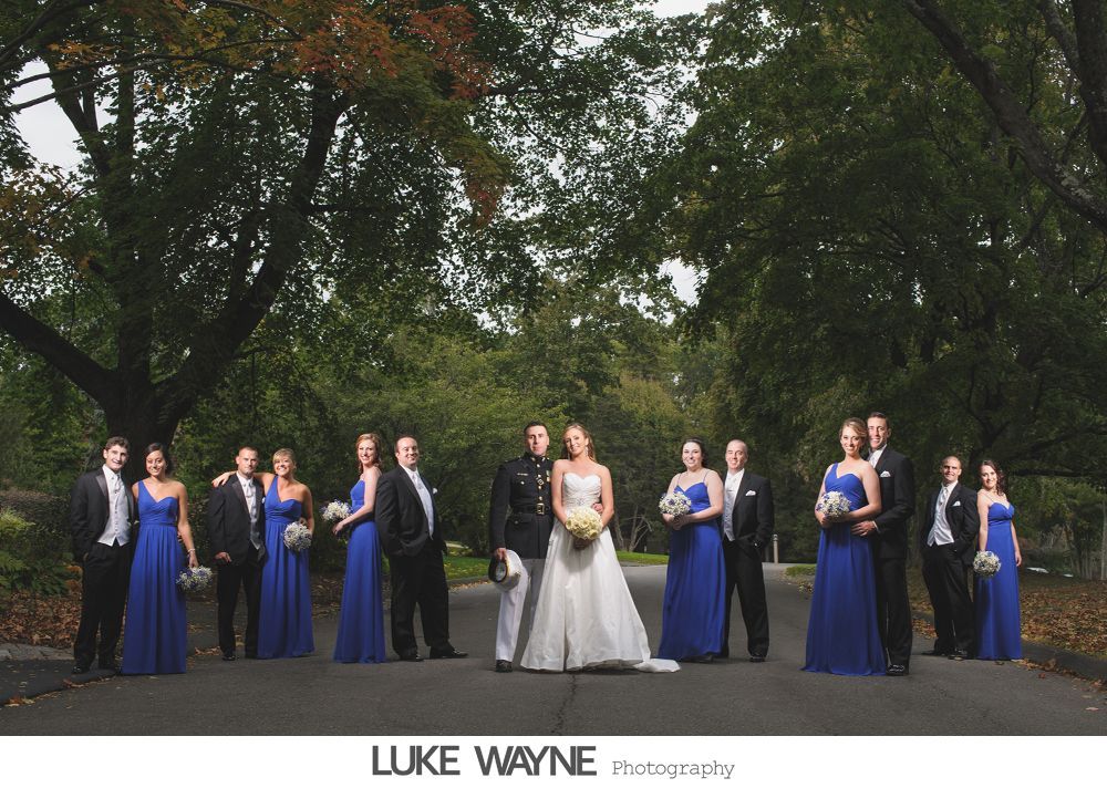 Man adjusting shirt cuffs, then smiling, wearing a gray suit with lavender bow tie and pocket square.