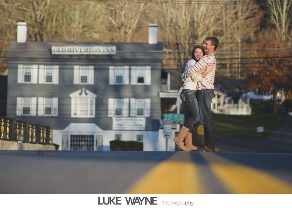 Bride in strapless white dress holding purple flowers, smiling. Dark background with archway.