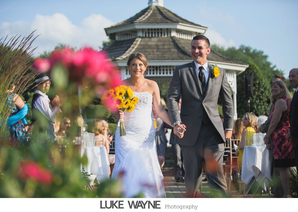 Wedding party toasting with champagne in a dimly lit bar, bride and groom center. Purple dresses, grey suits.