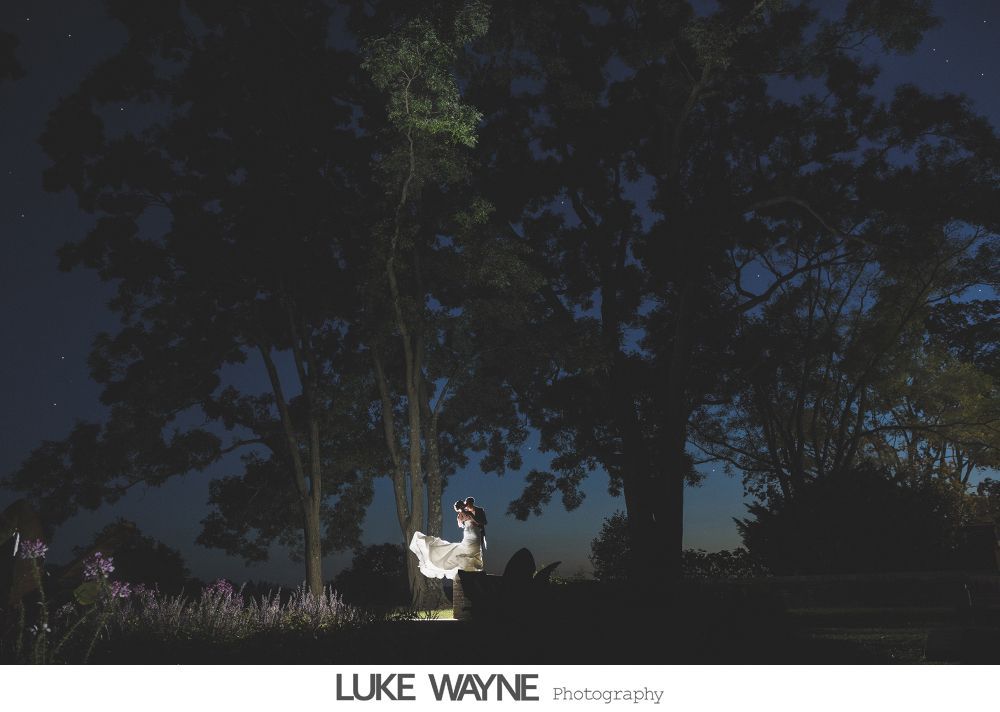 Couple in wedding attire posing in a bar. The woman's dress is white, the man's suit grey, both smiling.
