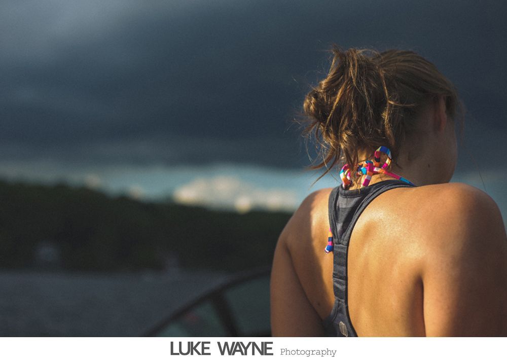 Bride and groom exit a building, holding arms, smiling. Bright sun streams through windows.