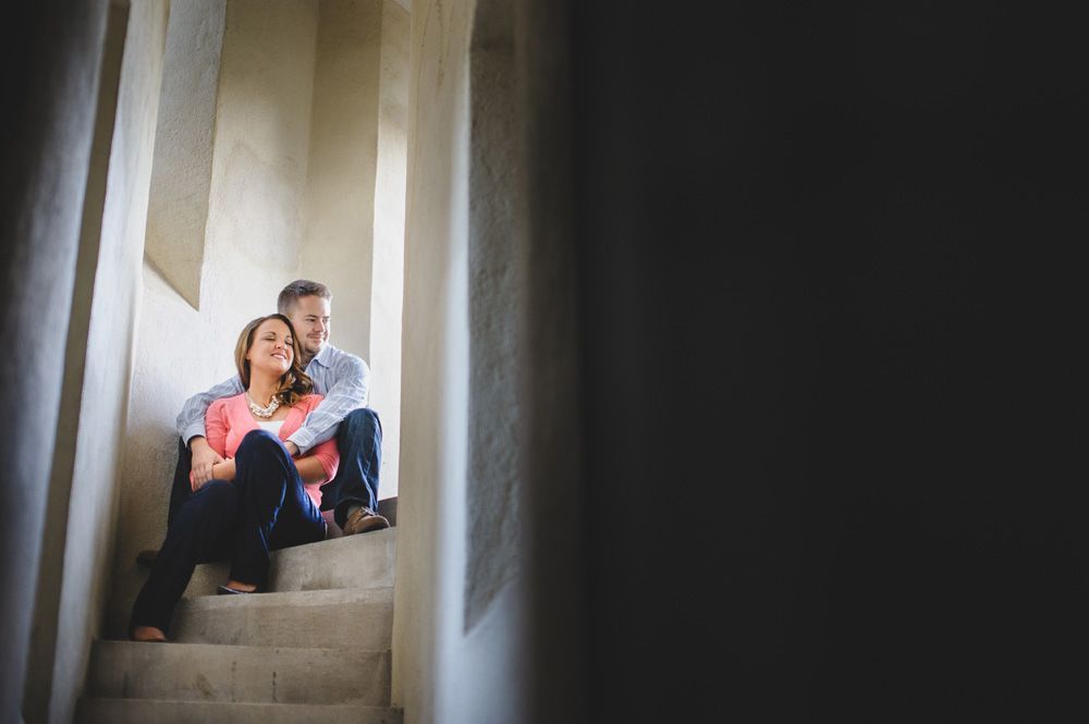 Couple sitting on stone steps in a dimly lit hallway; woman in pink, man in blue, smiling.