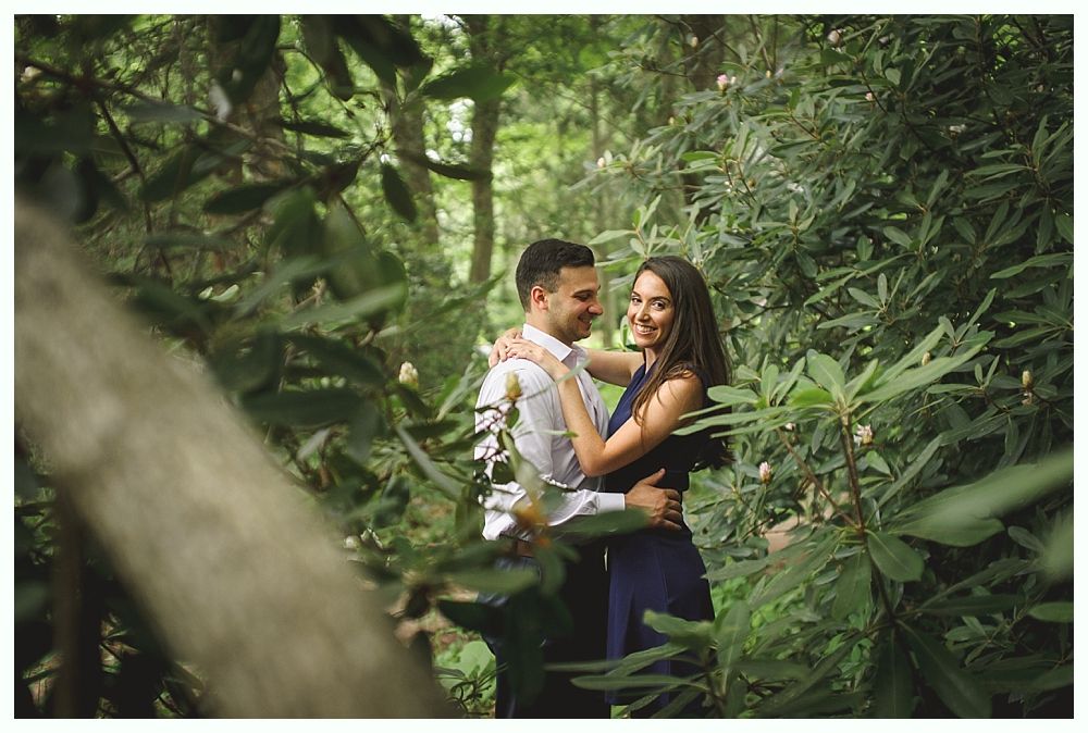 Man adjusting tie, another man in background near a window. Black and white.
