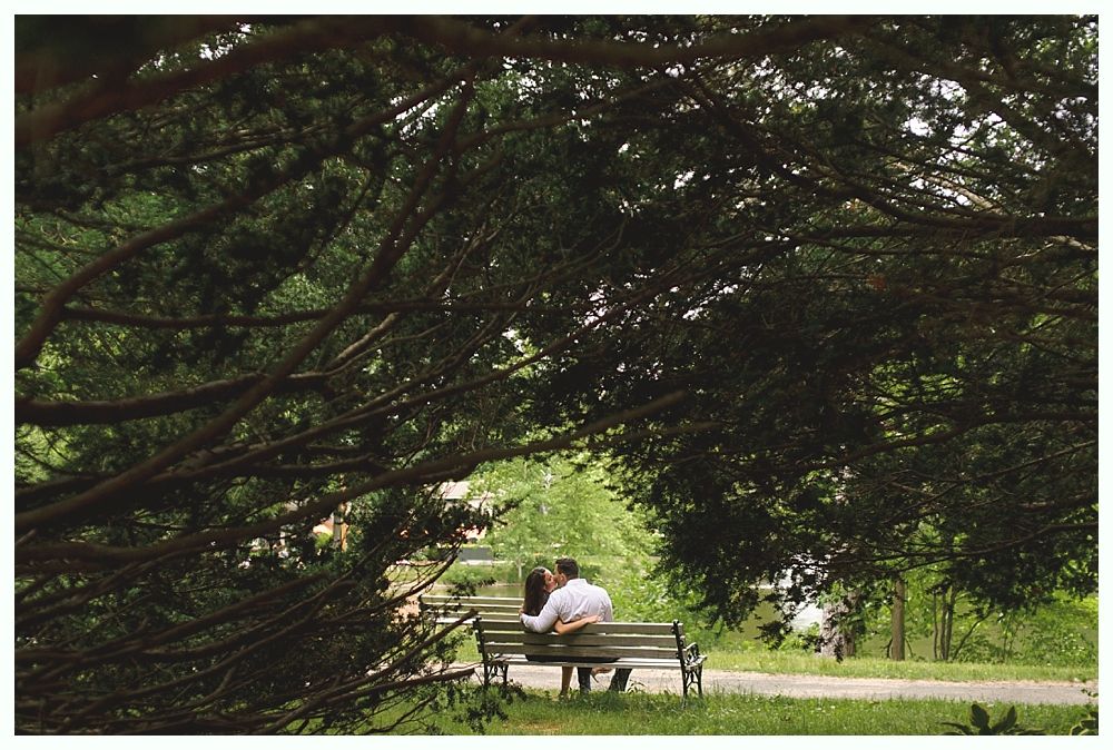 Bride in white lace wedding dress holding bouquet, smiling, by window.