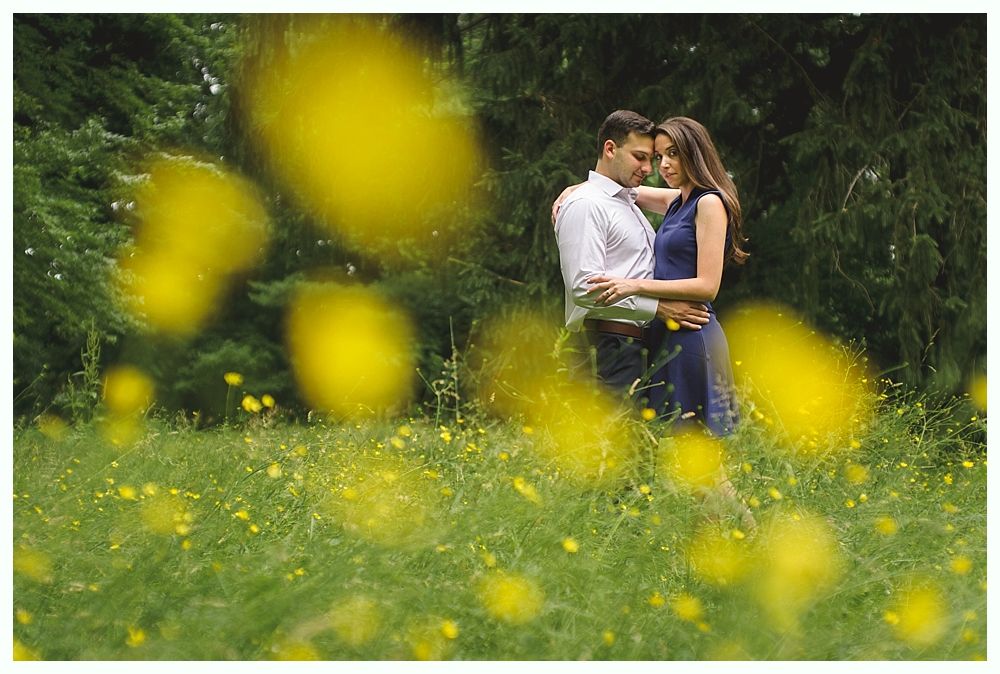 Groom smiles at camera on a bridge. Bride and bridesmaids pose, adjusting the wedding dress. Colorful flowers decorate the bridge.
