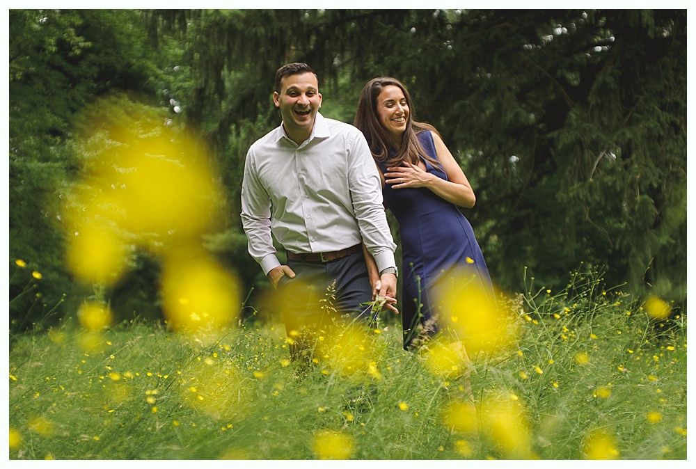 Bride and groom on a bridge. She touches his face, laughing. Surrounded by hanging flower baskets.