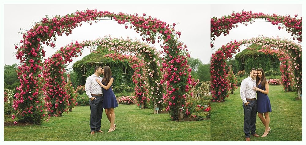 Bride and groom embrace on wooden bridge lined with flowers, house in background.