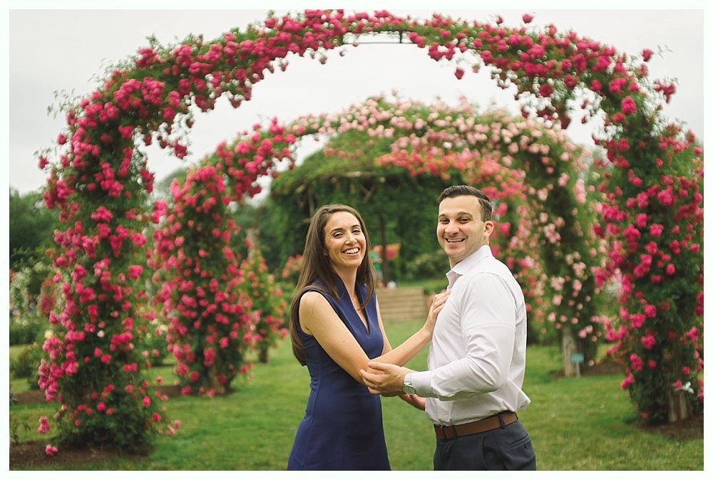 A newly married couple poses on a bridge and in front of a building; the woman wears a white gown, and the man wears a blue suit.