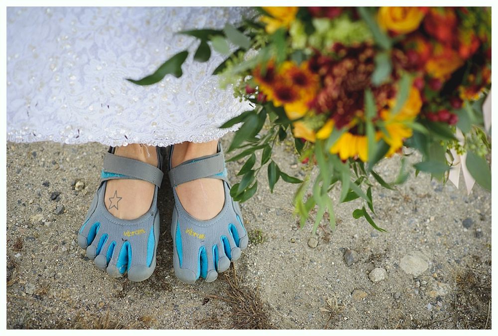 Bride's feet in blue toe shoes beneath a white dress, holding a colorful bouquet, standing outdoors.
