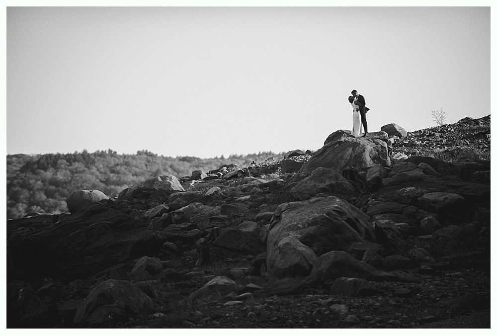 Couple embracing on rocky hilltop overlooking forest. Black and white.