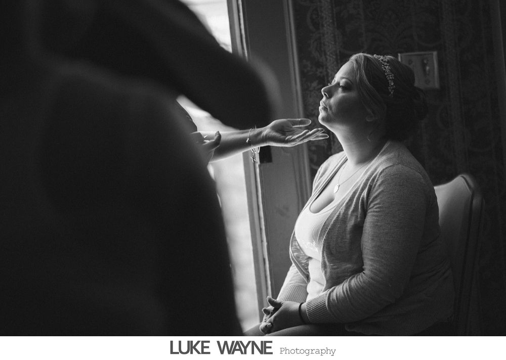Woman has makeup applied next to window, wearing a light sweater and a headband.