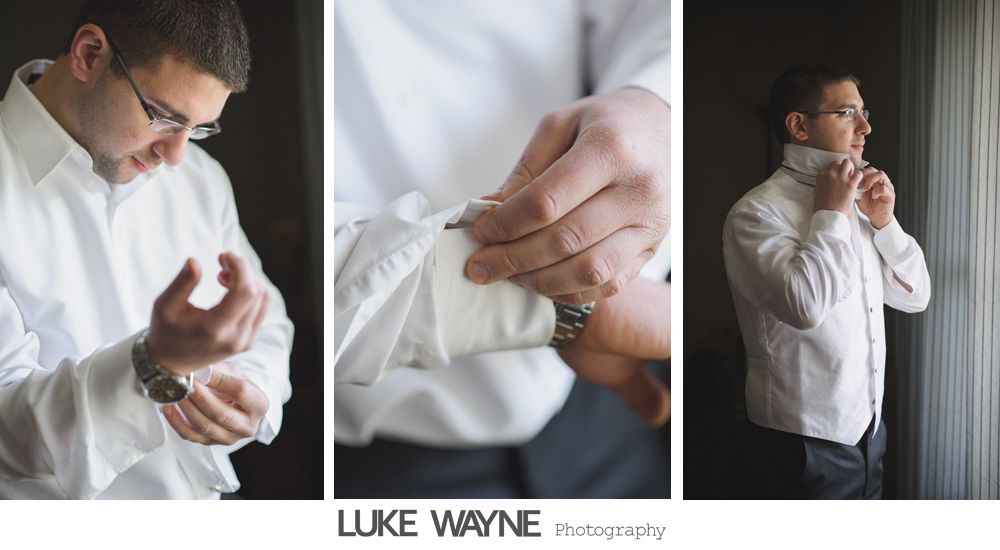 Man in white shirt getting dressed, adjusting cufflinks and collar in a bright room.