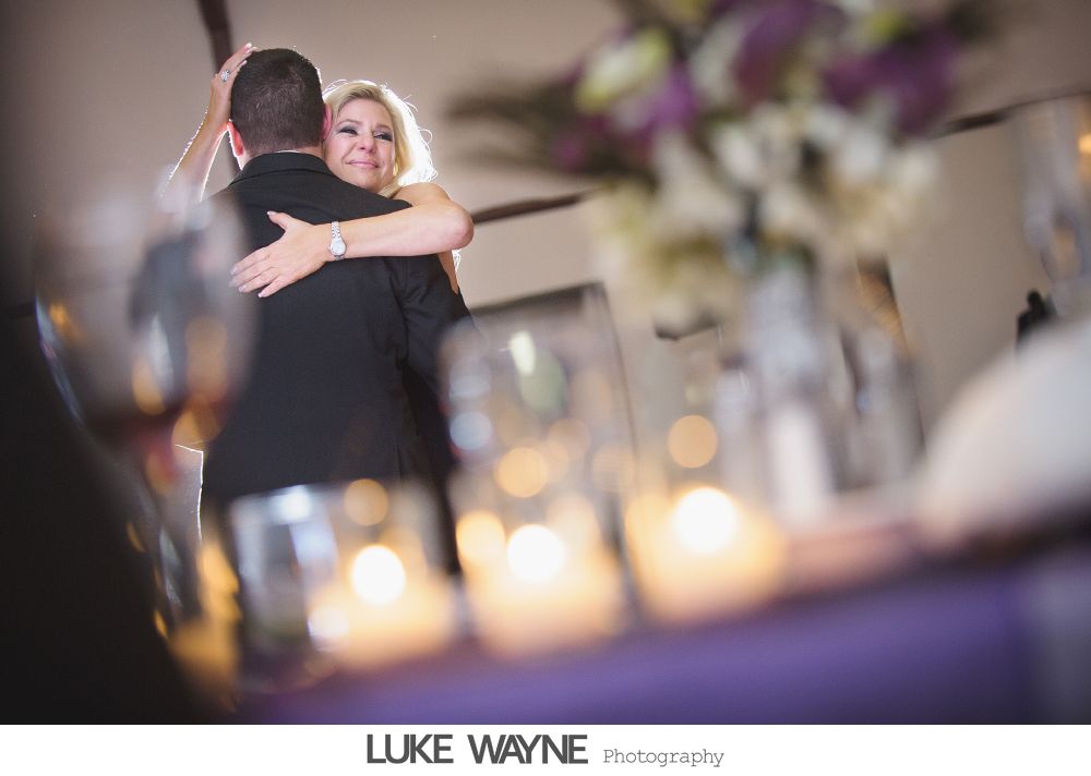 Bride and groom embrace on a dance floor, candles in foreground, flowers in background.