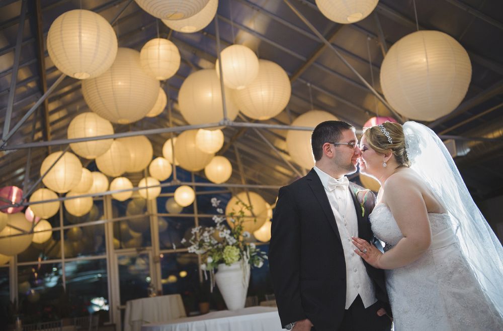 Couple kissing at wedding reception under paper lanterns.