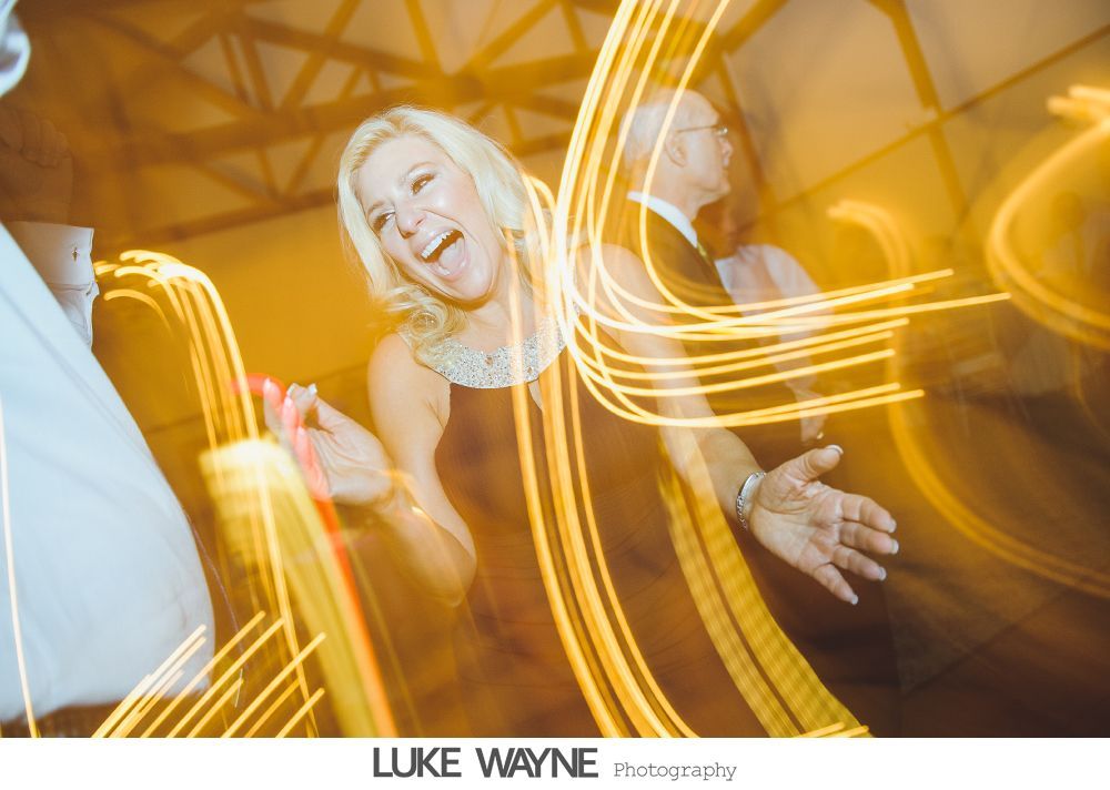 Woman dancing at an event, wearing a dark dress. Yellow light streaks create motion blur effect.
