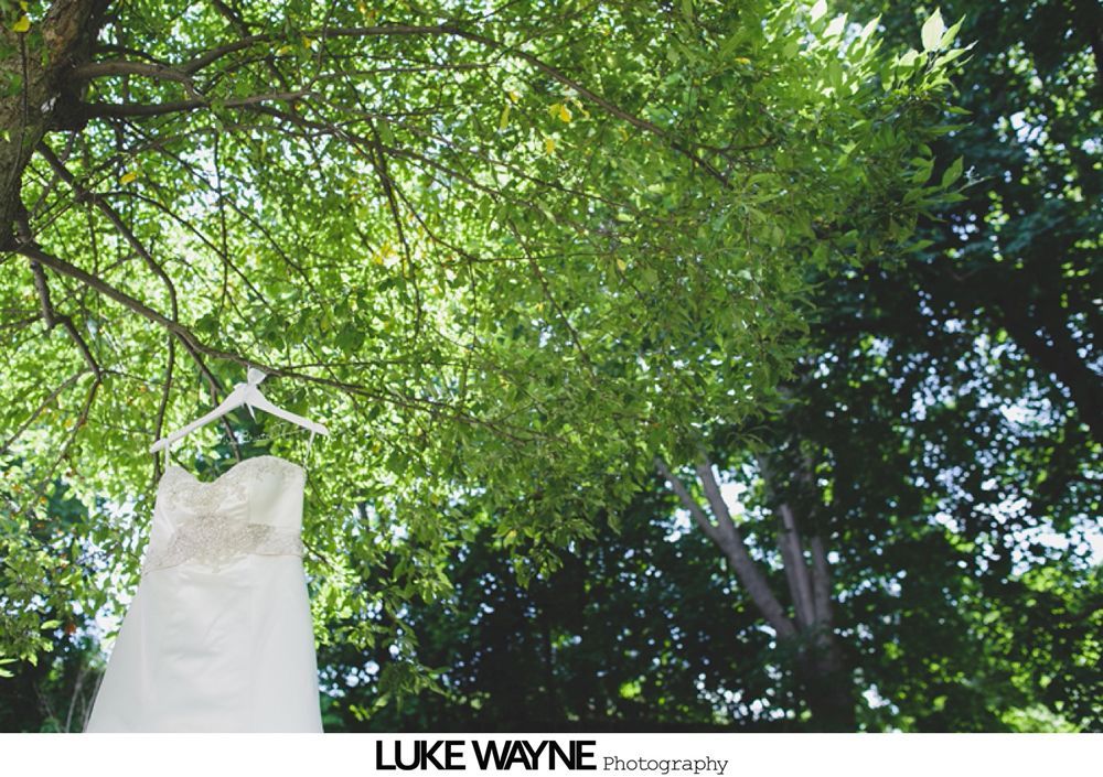 Man in gray suit with bow tie and boutonniere, smiling, outside near an old vehicle.