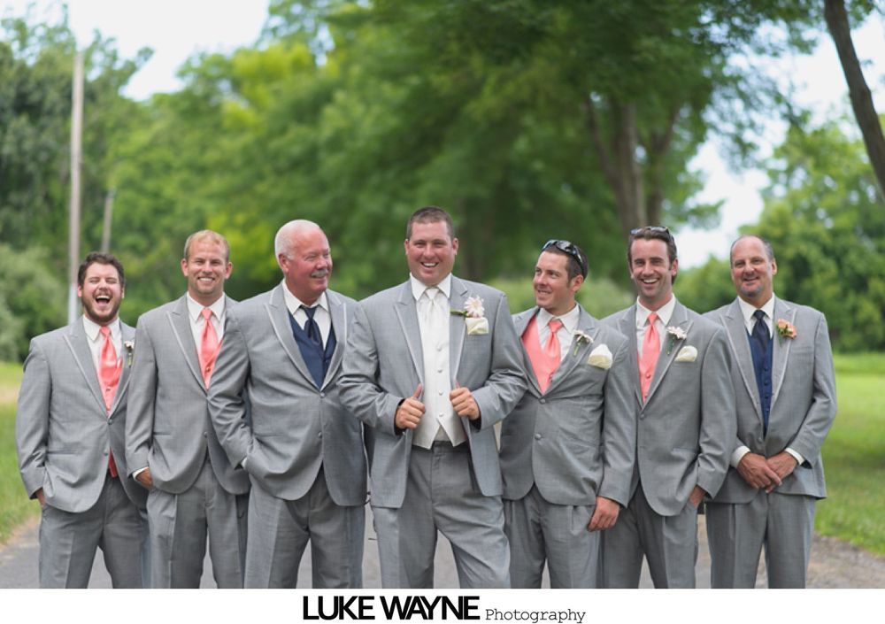 Seven men in gray suits pose outdoors; some smiling, some with hands in pockets.