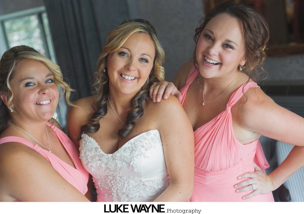 Bridesmaids in pastel dresses and bride in white, walking down a road, holding bouquets, sunny day.