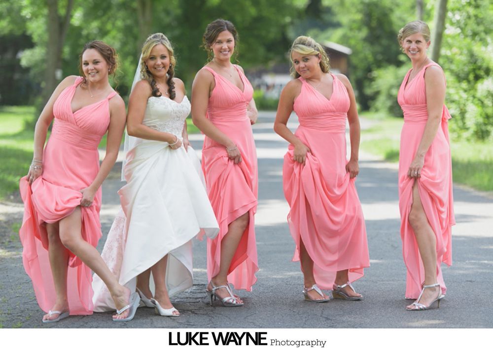 Bridesmaids in pastel dresses hold bouquets, posing outside a building next to a sign for the Hill-Stead Museum.