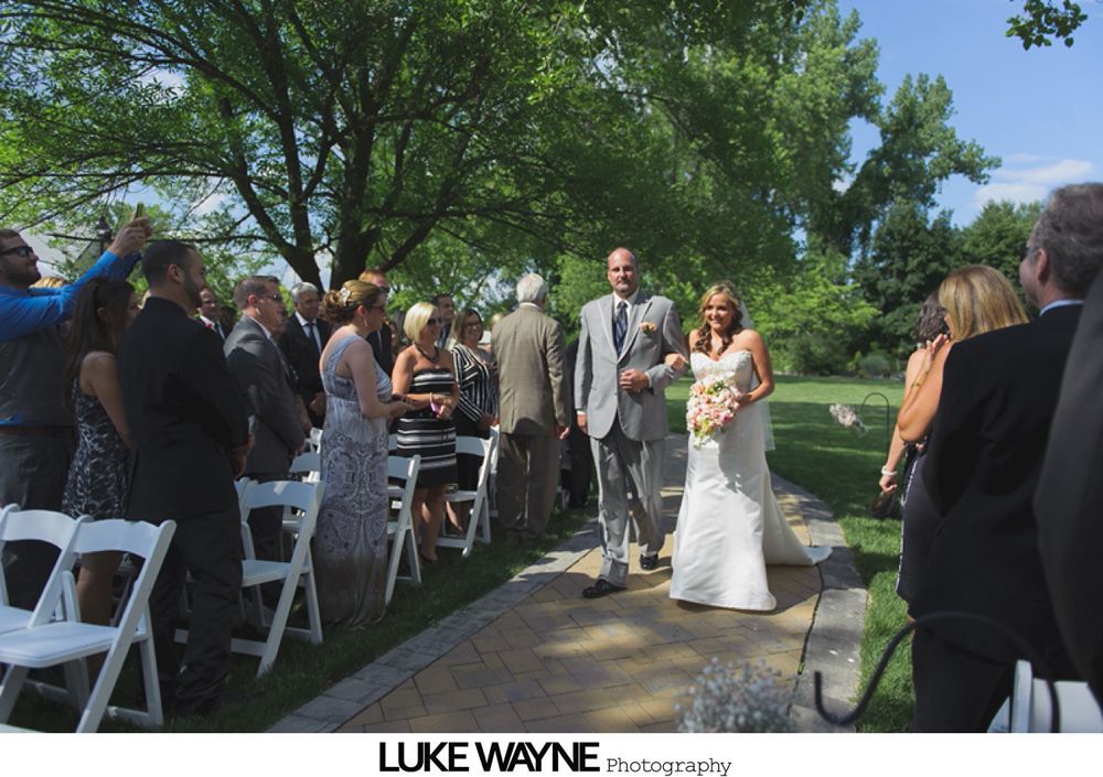 Bride in a white lace wedding dress holding a bouquet. She's outdoors on a pathway, smiling.