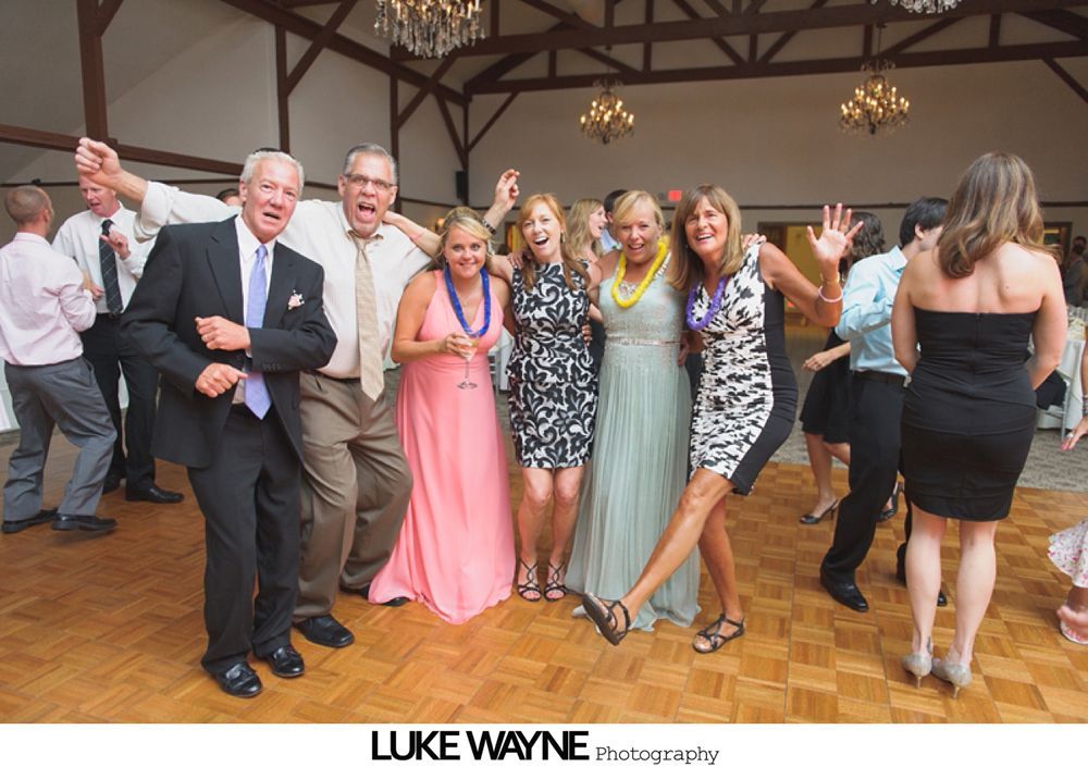 Group photo at a wedding reception. Bride and groom centered, surrounded by guests in formal attire.