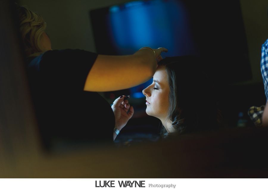 Makeup artist applying makeup to a person's face indoors, illuminated by a light.