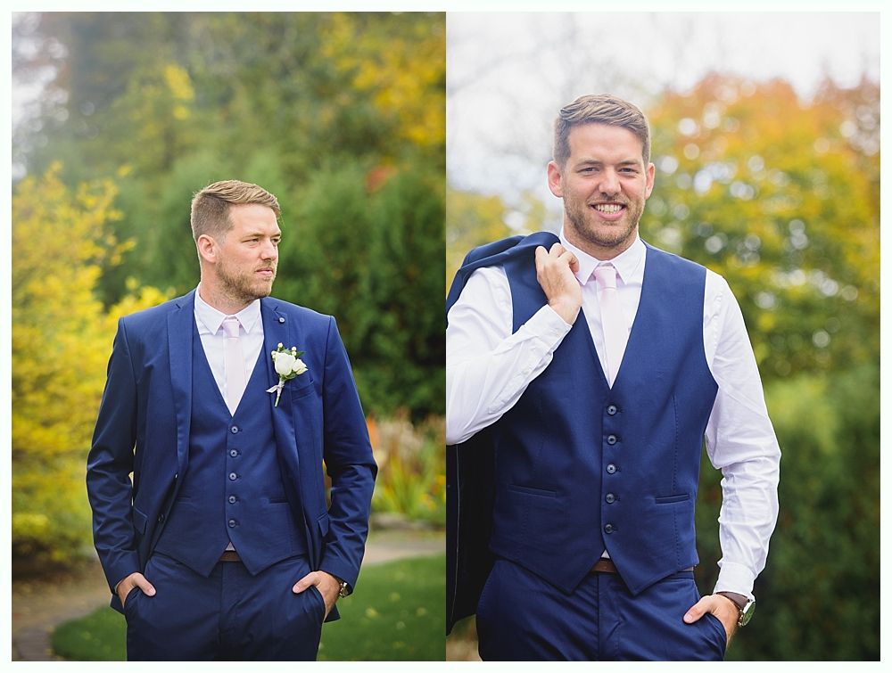 Man in a blue suit, posing in a garden. He has short blonde hair and a white shirt.