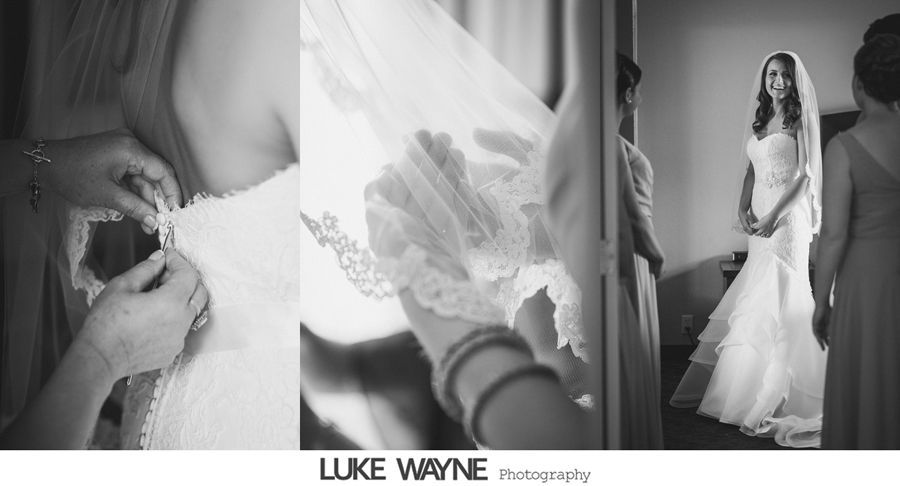 Wedding dress being buttoned up, bride wearing veil, standing near bridesmaids in a room.