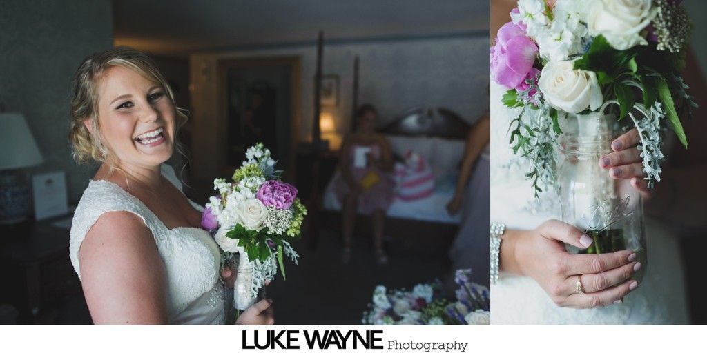 Bride holding bouquet, smiling in a room. Bridesmaids in the background.