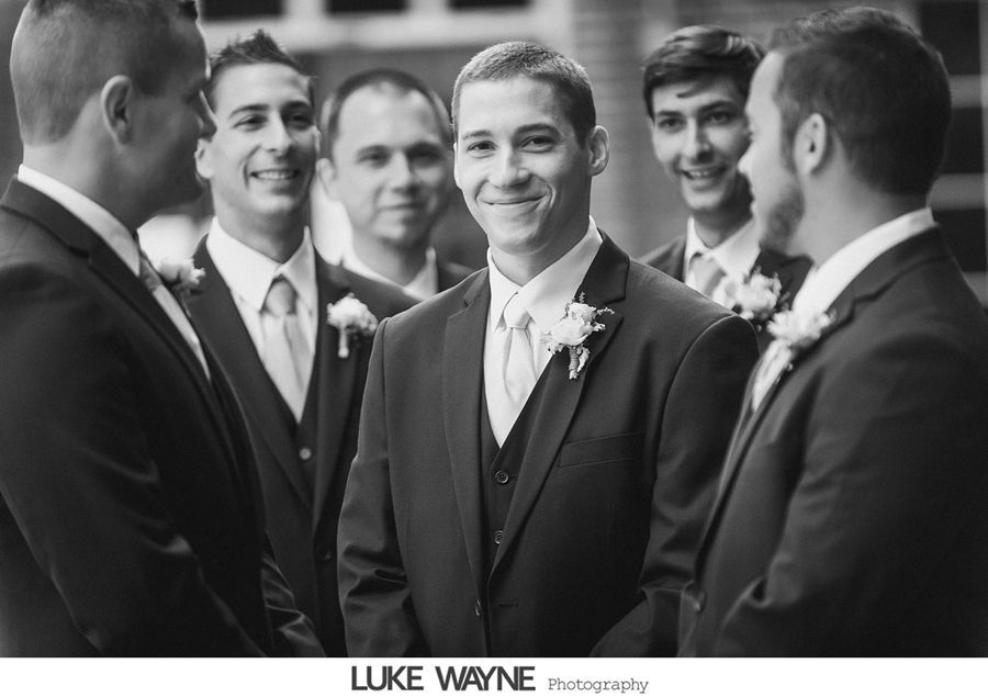 Groom and groomsmen in suits smiling outdoors. Black and white photograph.