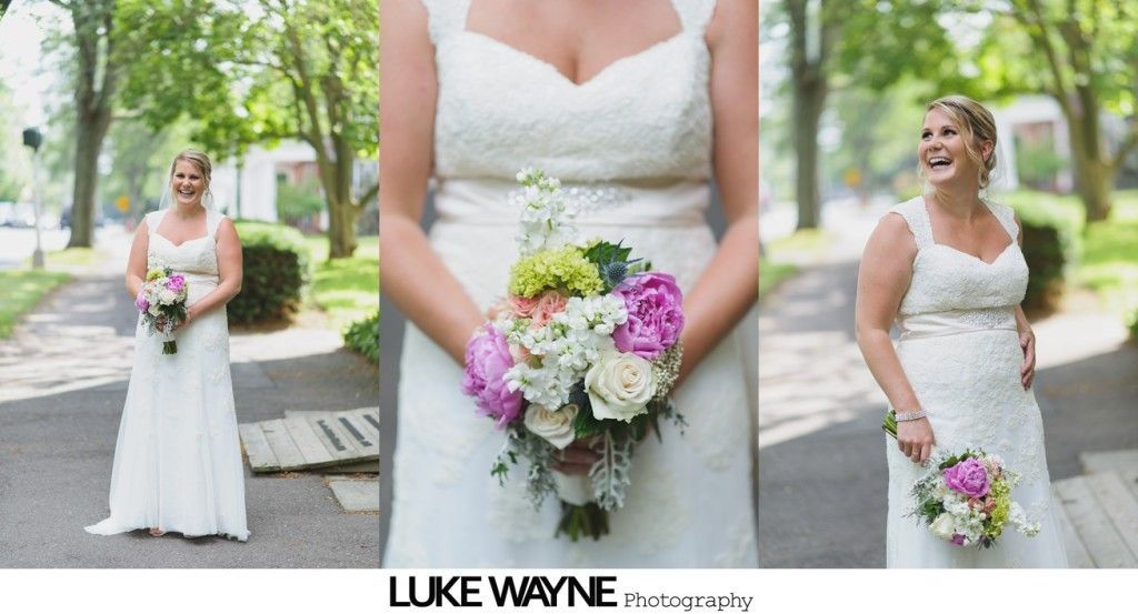 Bride in a white lace wedding dress holding a bouquet. She's outdoors on a pathway, smiling.