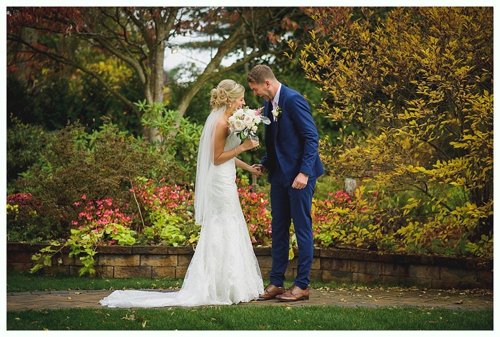 Bride and groom in formal attire, holding flowers, embrace in a garden.