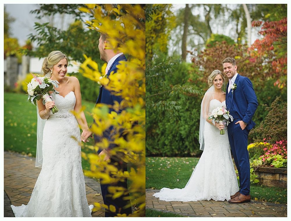 Bride and groom holding hands, smiling, in a garden. The bride wears a white dress, the groom a blue suit.