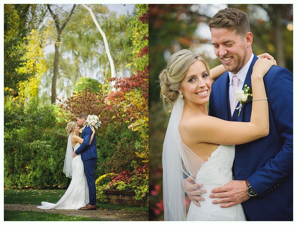 Bride and groom embrace, one kissing. Outdoor wedding setting with trees and flowers. The couple smiles joyfully.