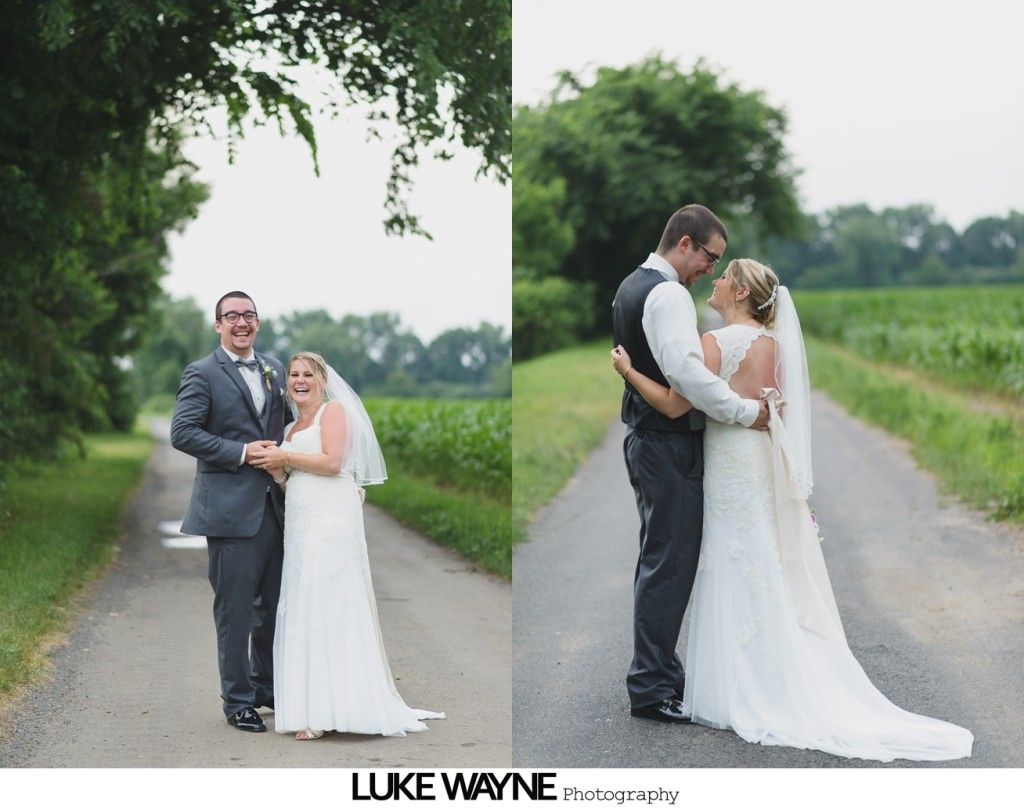 Wedding couple embracing on a rural road; the bride wears a white dress and veil, the groom in a suit and vest.