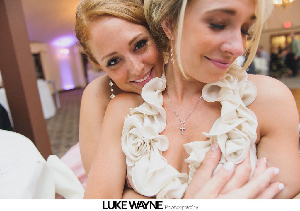 Woman embracing another, both smiling; indoors, event setting.