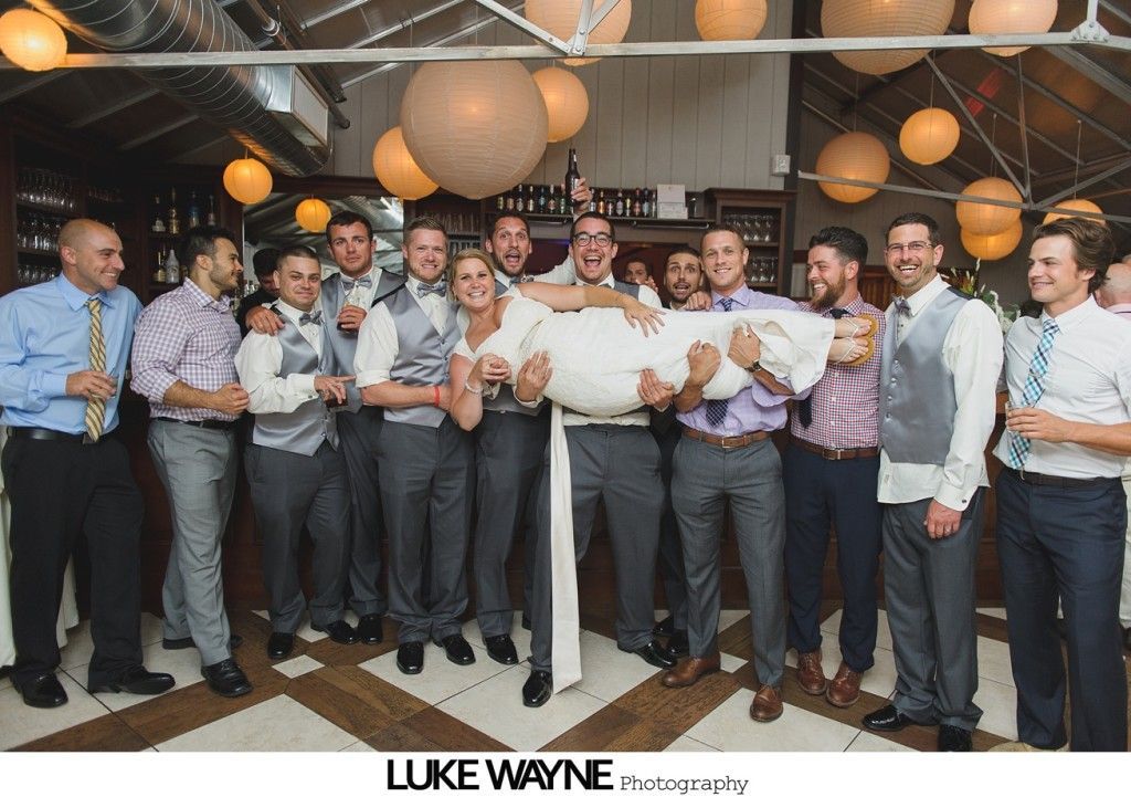 Wedding party carrying bride indoors with paper lanterns.