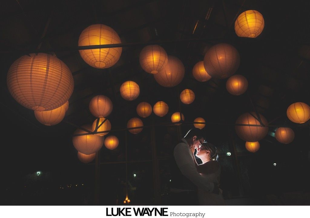 Couple embracing beneath glowing orange paper lanterns at night.